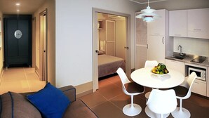 A compact living space with a kitchenette, a dining area with a fruit bowl, and a bed in the background. - Cala Del Porto 2-room-apartment 3P (Marettimo)