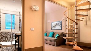 A spiral staircase with a wooden finish, a living area with a sofa and teal cushions, and a patterned floor. - Cala Del Porto 2-room-apartment 3P (Marettimo)