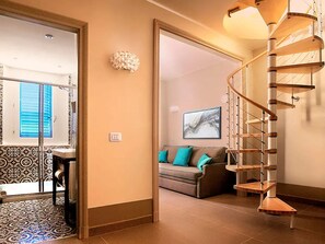 A spiral staircase with a wooden finish, a living area with a sofa and teal cushions, and a patterned floor. - Cala Del Porto 2-room-apartment 3P (Marettimo)