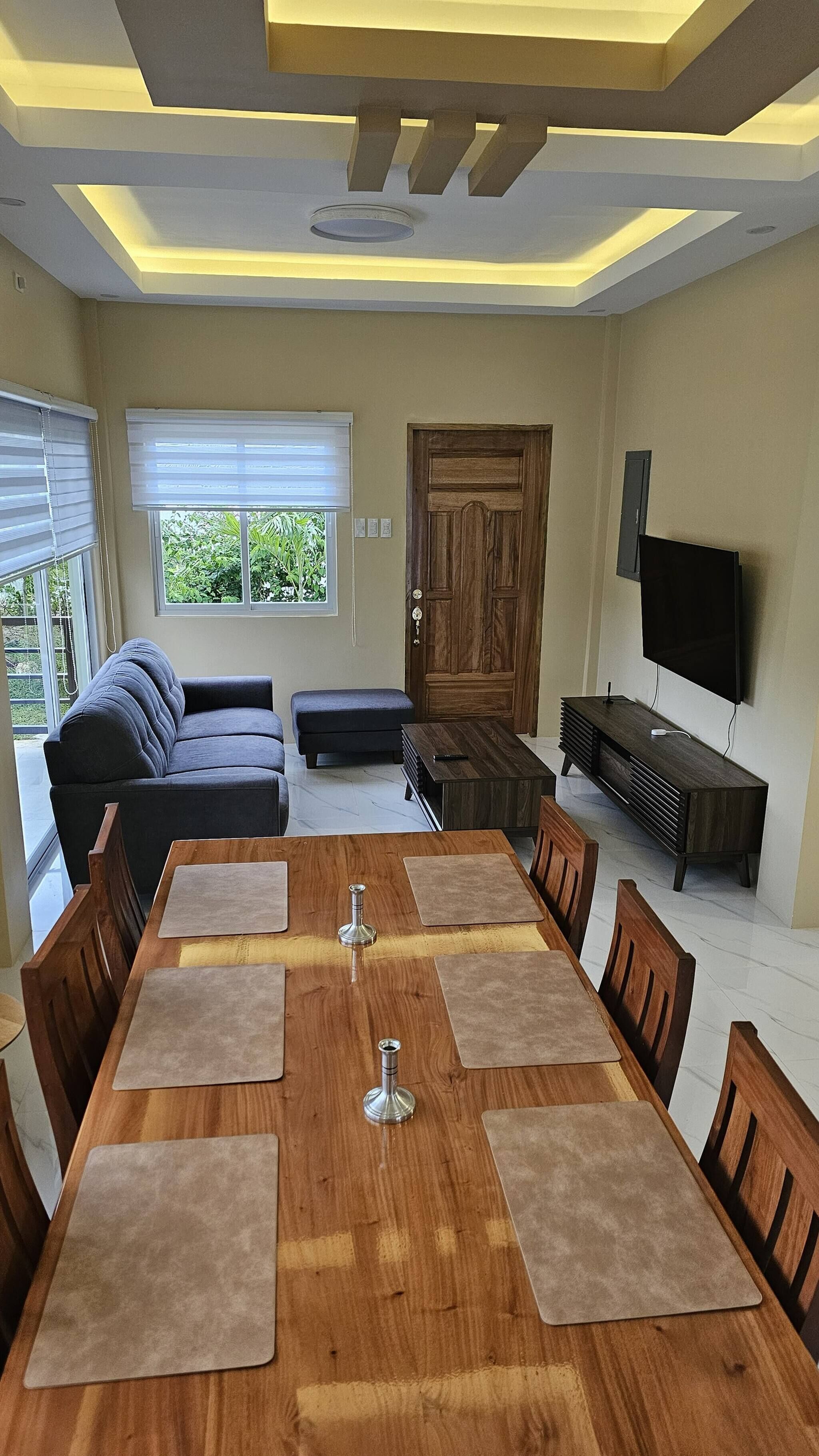 Un salon moderne comprenant une table à manger, des canapés, un téléviseur et une porte en bois.