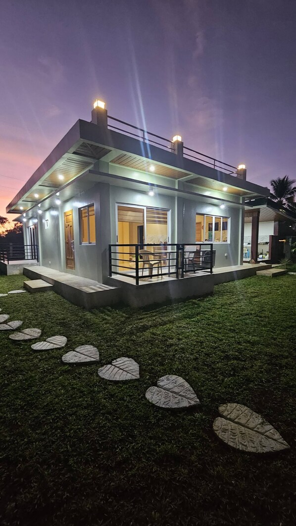 A modern house with a covered patio, a well-lit entrance, and a grassy yard with decorative leaf patterns.