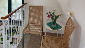 Ein Balkon mit Korbstühlen, einem kleinen Tisch und einem Blumenvasen sowie einem weißen Geländer.