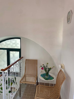 Ein Balkon mit Korbstühlen, einem kleinen Tisch und einem Blumenvasen sowie einem weißen Geländer.
