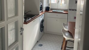 Eine kleine Küche mit Waschmaschine, Spüle und einem Fenster mit Vorhang.