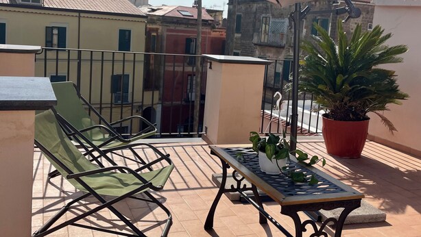 Eine Terrasse mit Tisch, Stühlen, einer Kübelpflanze und einem großen Sonnenschirm.