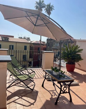 Eine Terrasse mit Tisch, Stühlen, einer Kübelpflanze und einem großen Sonnenschirm.