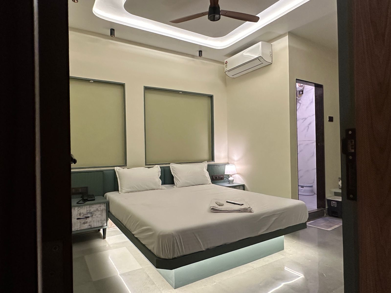 A modern bedroom with a bed centered under a ceiling fan, air conditioning units, and a nightstand with a lamp.