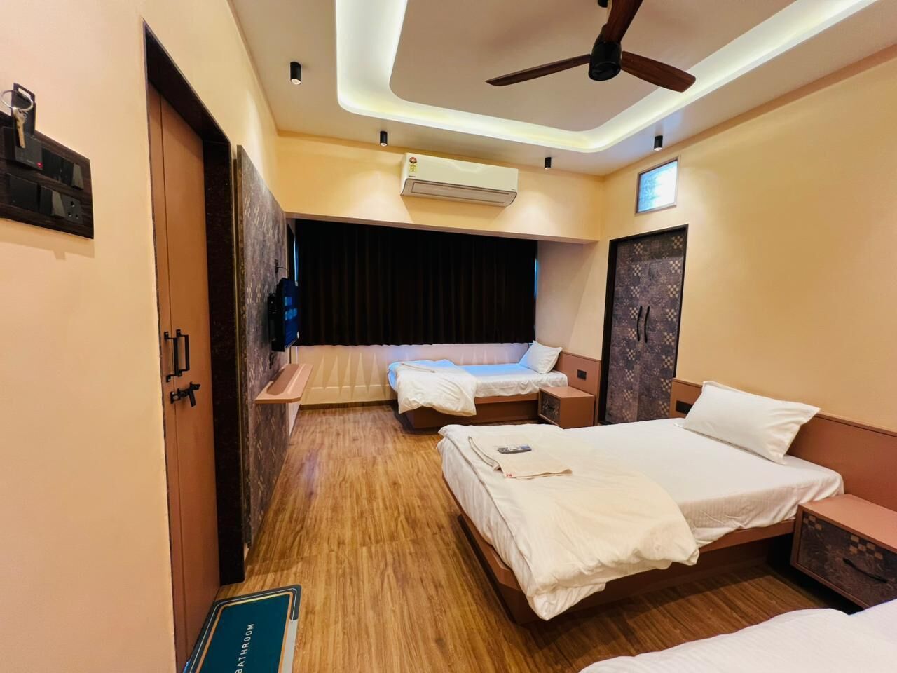 A hotel room with two beds, a ceiling fan, an air conditioning unit, a TV, and a wooden floor.