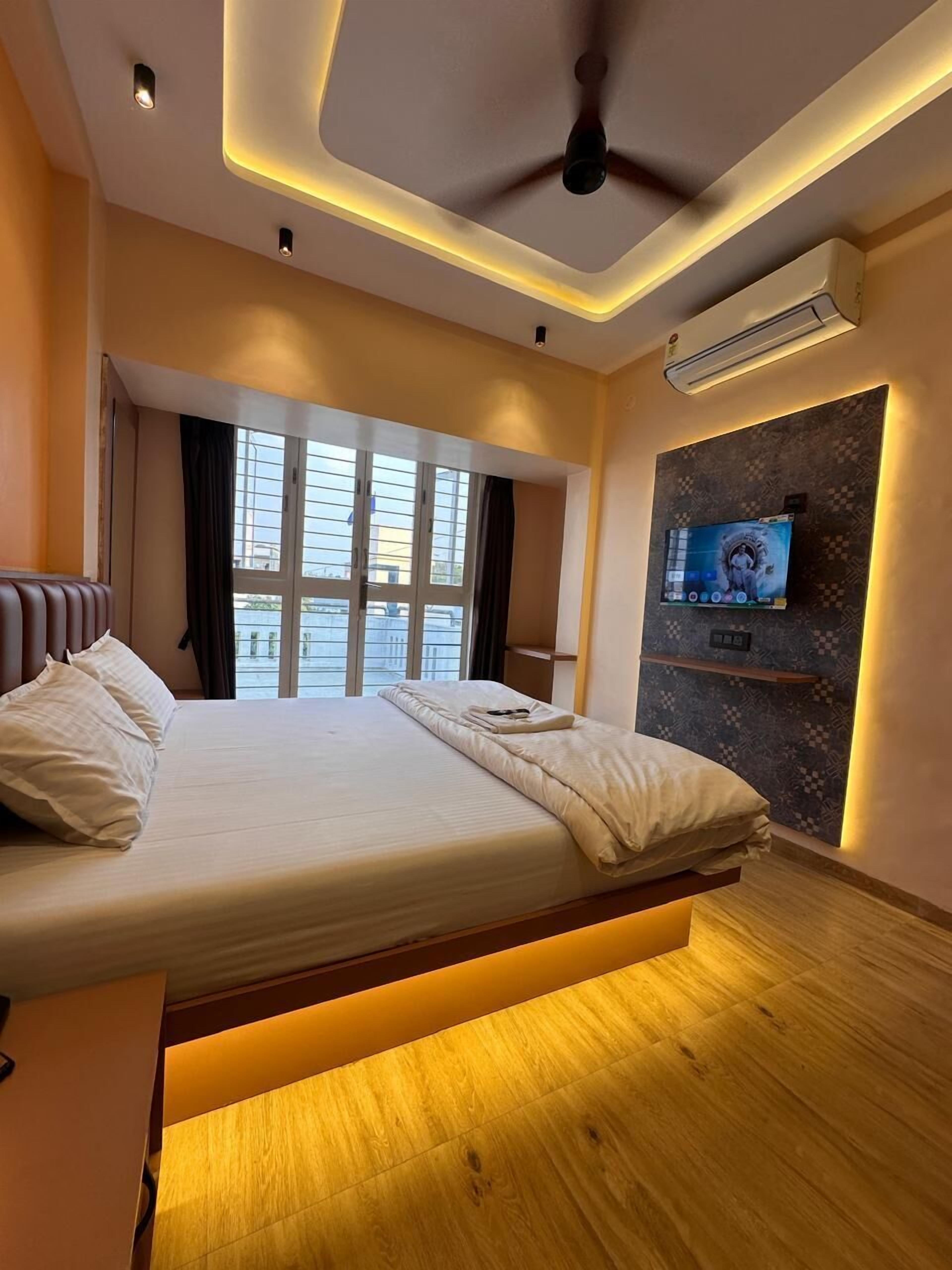 Une chambre d’hôtel moderne équipée d’un lit, d’un ventilateur de plafond, d’un appareil de climatisation, d’une télévision et de grandes fenêtres.