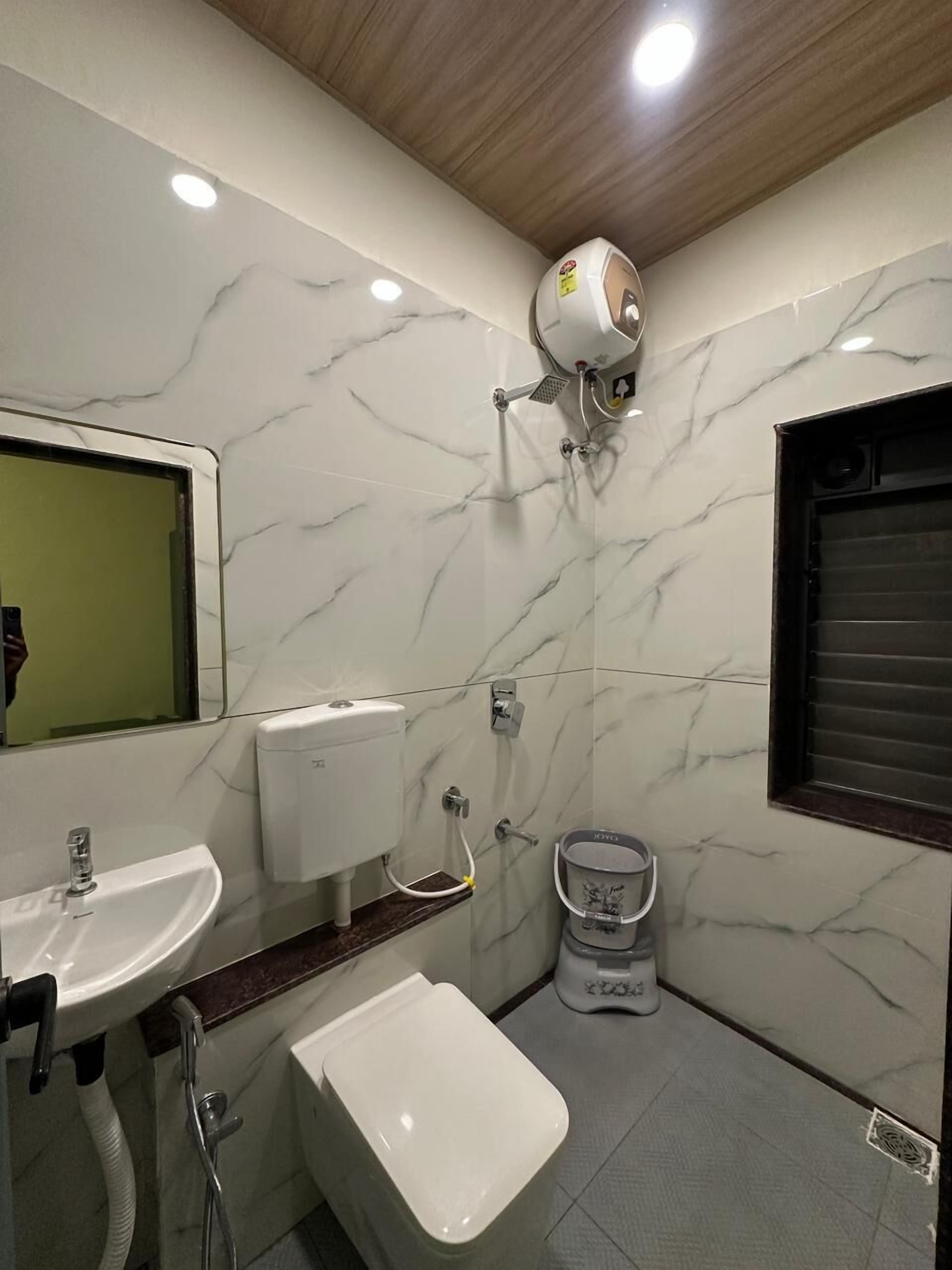 Une salle de bain avec un mur en marbre, des toilettes, un bidet, un lavabo et un miroir.