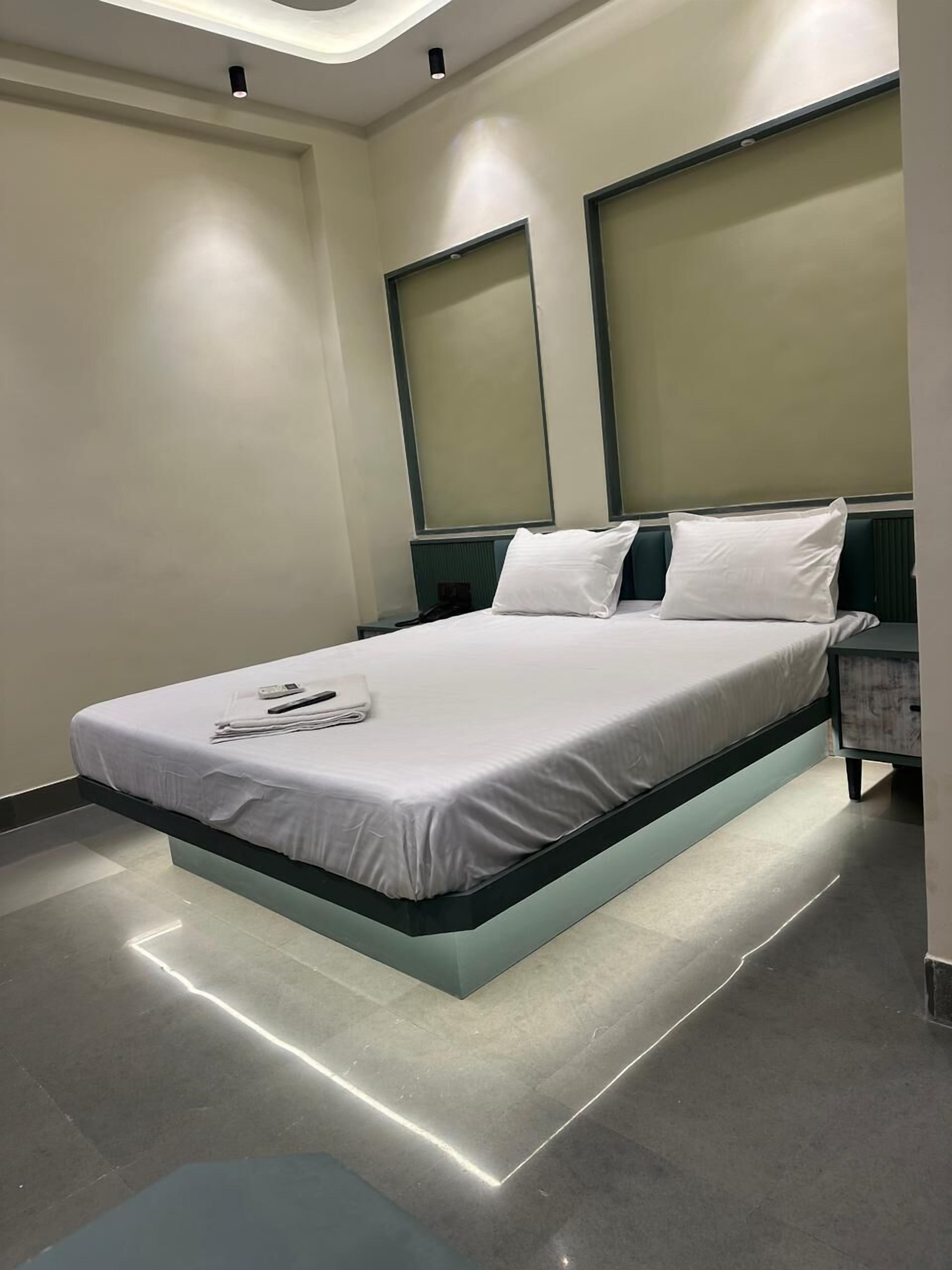 A modern hotel room with a central bed, a nightstand, and a built-in headboard.
