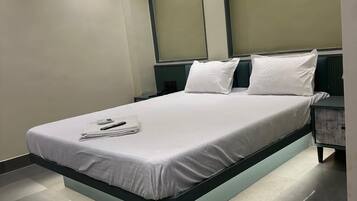 A modern hotel room with a central bed, a nightstand, and a built-in headboard.
