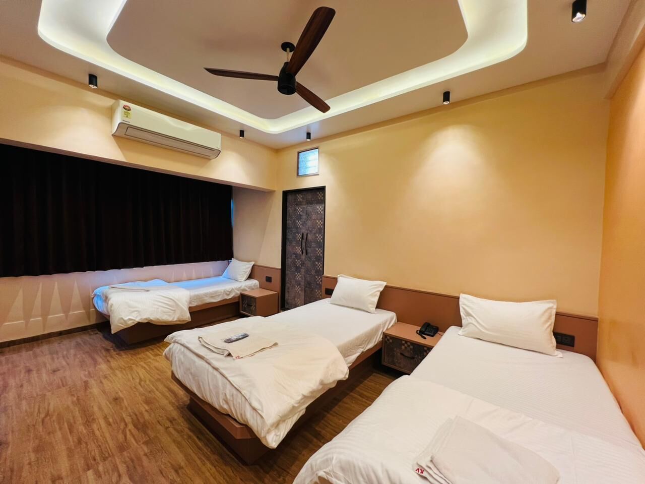 Habitación de hotel con tres camas, ventilador de techo, aire acondicionado y piso de madera.
