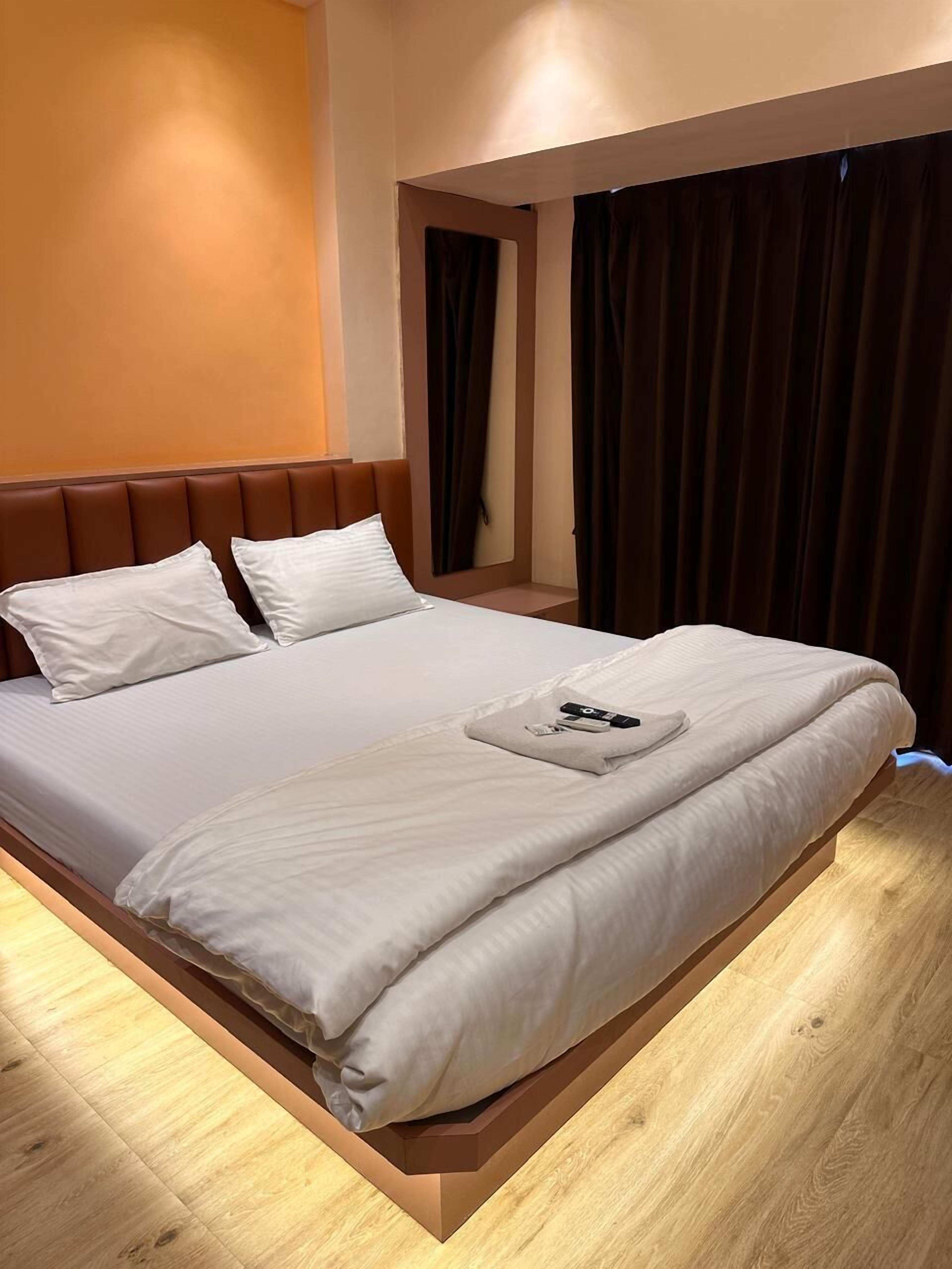 A hotel room with a bed, a headboard, a bedside table, and a window with curtains.