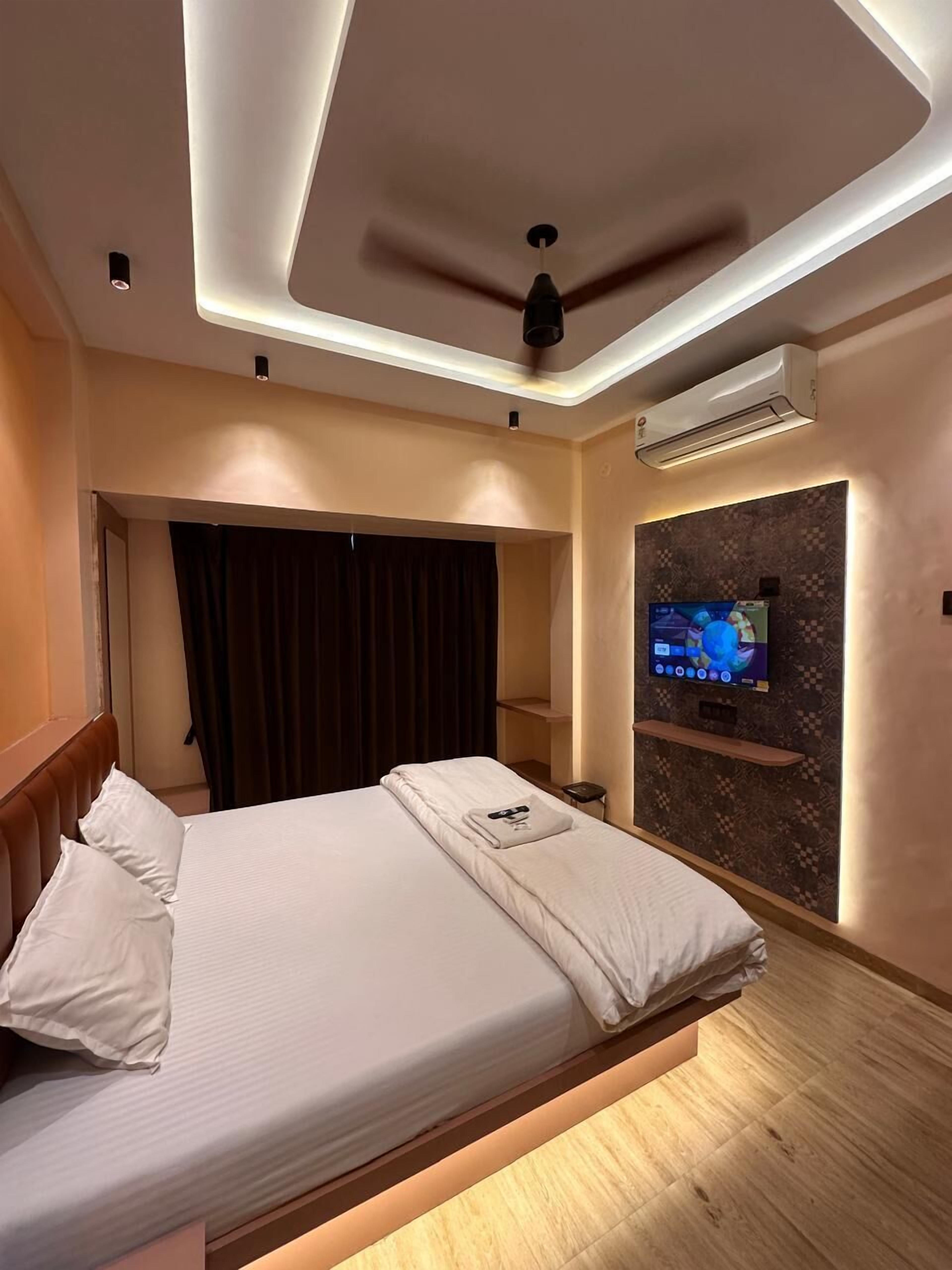 Een moderne hotelkamer met een bed, plafondventilator, airconditioning en een televisie, plus een wandplank.