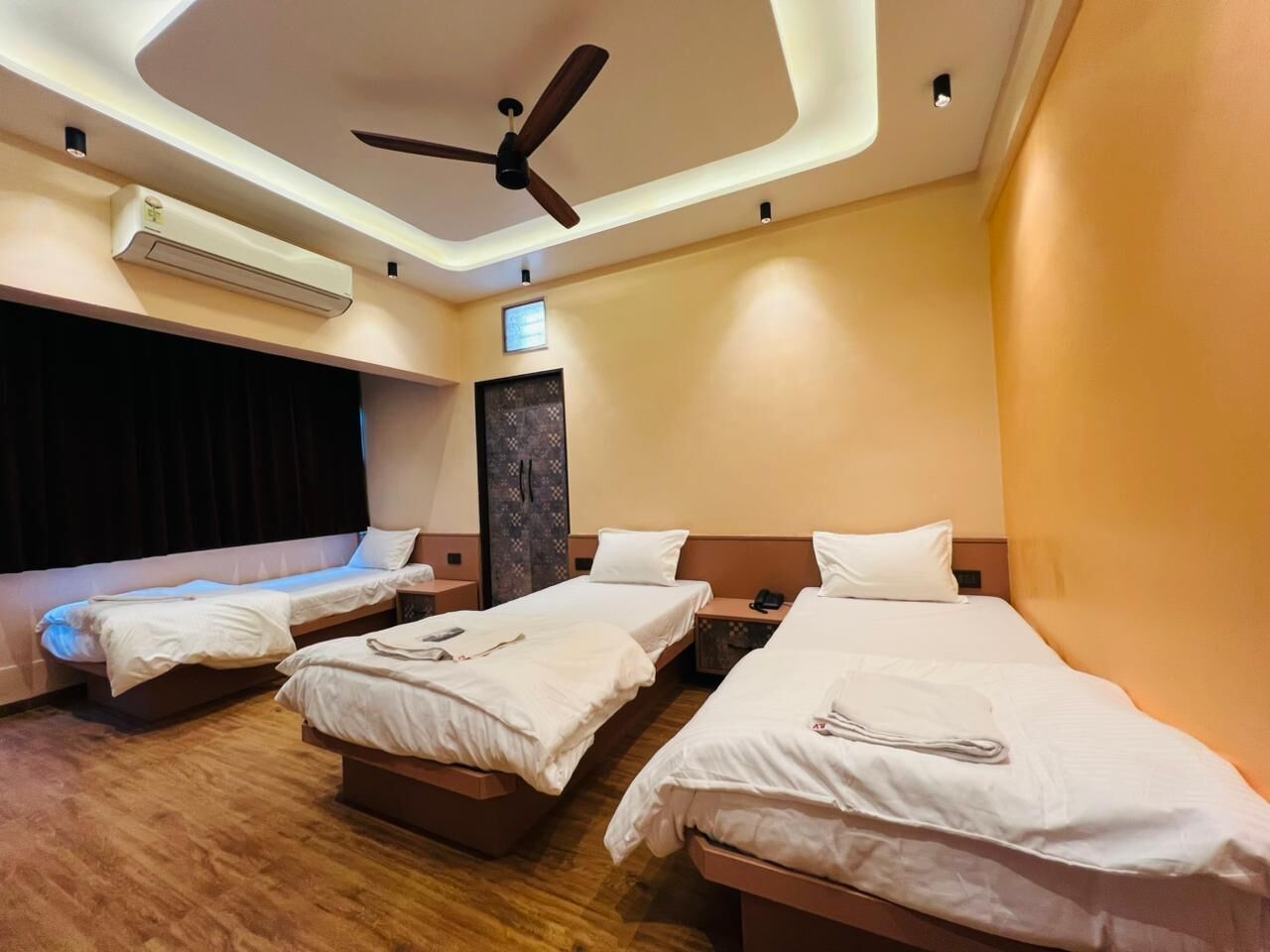 Een hotelkamer met drie bedden, een plafondventilator, een airconditioning en een kleine televisie.