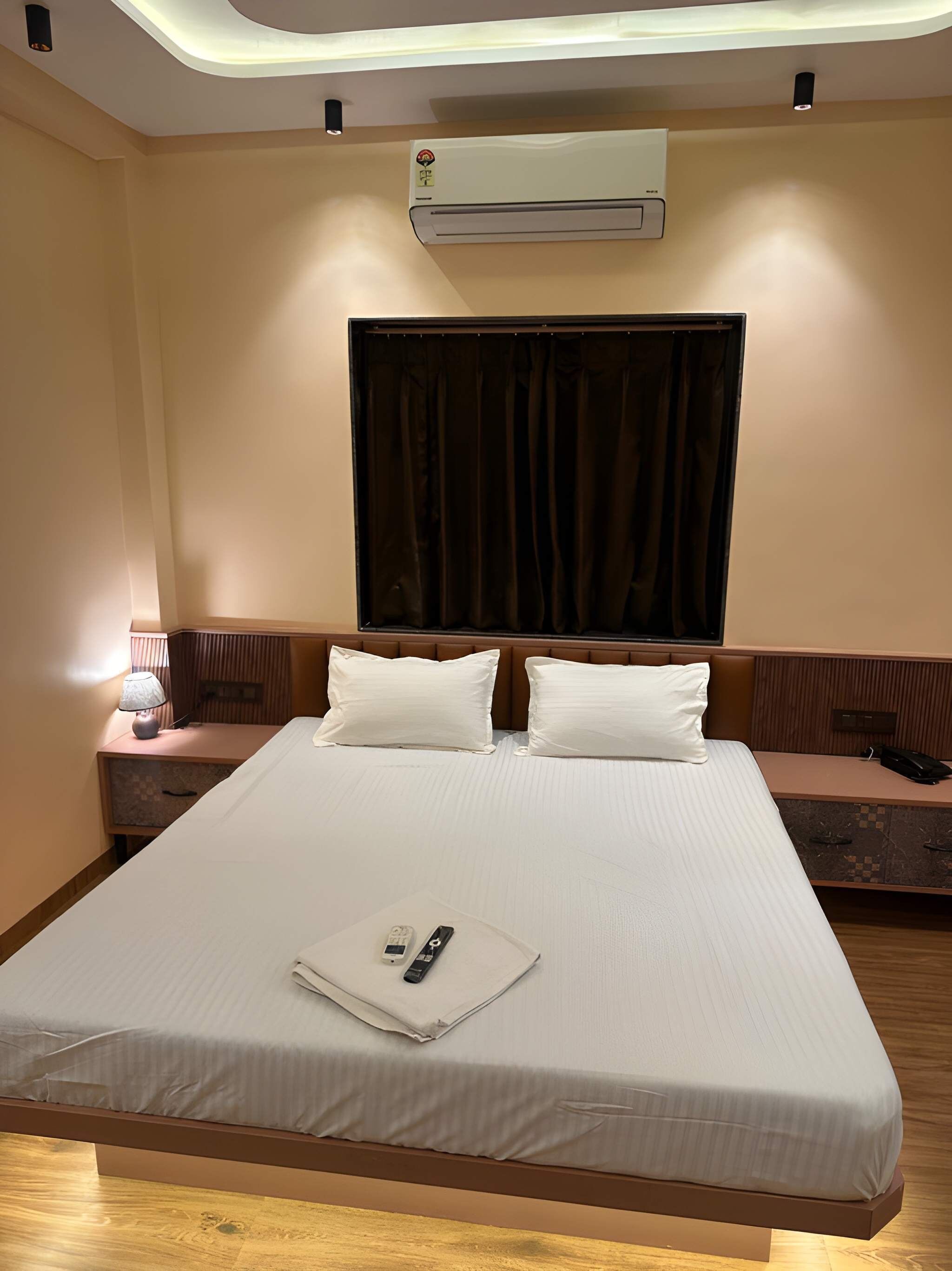 Habitación de hotel con cama, mesitas de noche, equipo de aire acondicionado y ventana con cortinas.