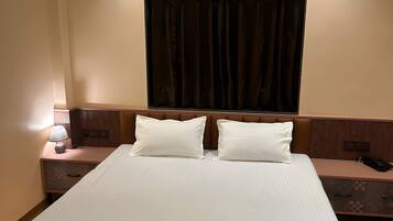 Habitación de hotel con cama, mesitas de noche, equipo de aire acondicionado y ventana con cortinas.