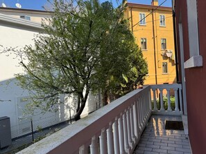 A balcony with a white balustrade overlooking a tree and a yellow building. - NK Venice Apartment (Venezia)