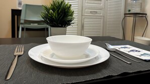 A dining setup with a bowl on a plate, a fork, and a spoon on a napkin, a potted plant, and a water dispenser in the background. - Olivia's BNB: Fully furnished private suite in Jimi Ameriya (Al Ain)