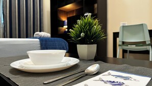 A hotel room with a dining table set with a white bowl, spoon, and a menu featuring fish illustrations. - Olivia's BNB: Fully furnished private suite in Jimi Ameriya (Al Ain)