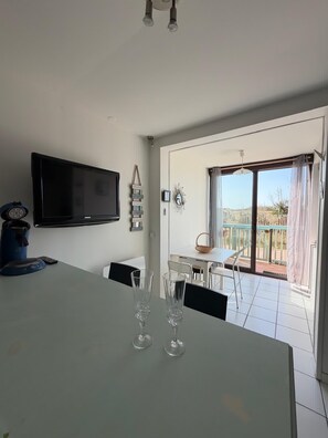 Una sala de estar moderna con un televisor de pantalla plana, una mesa de comedor con dos vasos y un balcón con mesa y sillas.