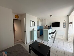 Een compacte woonruimte met kitchenette, een eethoek en een aan de muur bevestigde televisie.