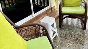 Huoneessa on tuoli ja pieni jakkara, ikkunassa metalliritilät ja ikkunasta näkyy ulkona olevia rakennuksia.