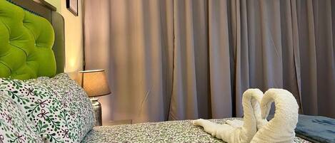 Habitación de hotel con cama, cabecera verde, lámpara y ventana con cortinas.