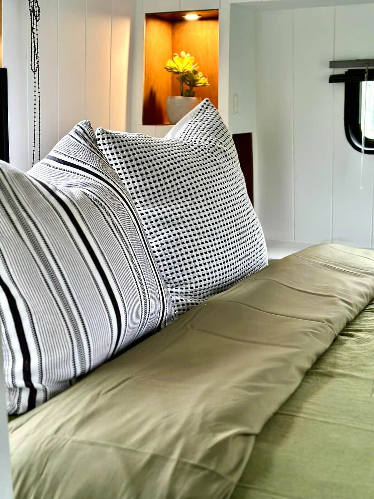 A bed with multiple pillows and a green bedspread in a room with white walls and a wooden accent wall.