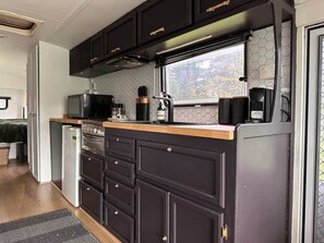 Una cucina compatta con mobili scuri, un forno a microonde, una macchina da caffè e una finestra vista verde.