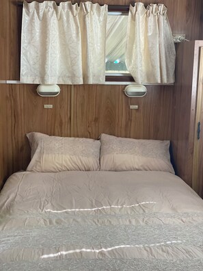 A bed with a headboard, two pillows, and a window with curtains.
