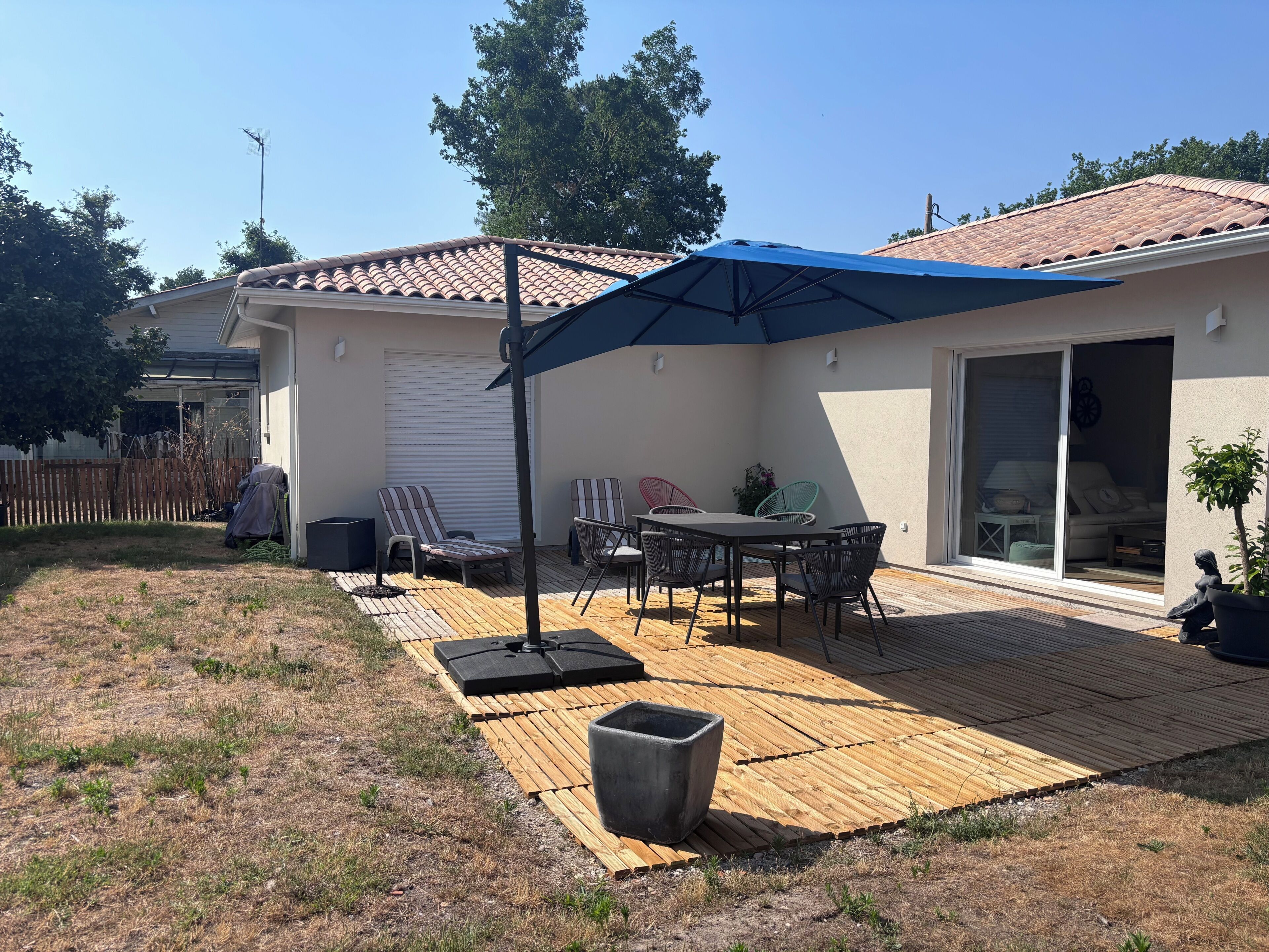 Une terrasse avec une table et des chaises, un parasol et une porte-fenêtre coulissante donnant sur un espace intérieur.