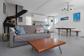 A modern living room with a sofa, coffee table, dining area, kitchen, and staircase. - Cosy house 6 pers near beaches, south facing (Quiberon)
