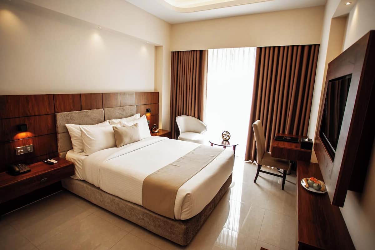 A hotel room with a large bed, a desk, a chair, a TV, and a window with curtains.