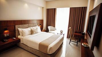 A hotel room with a large bed, a desk, a chair, a TV, and a window with curtains.