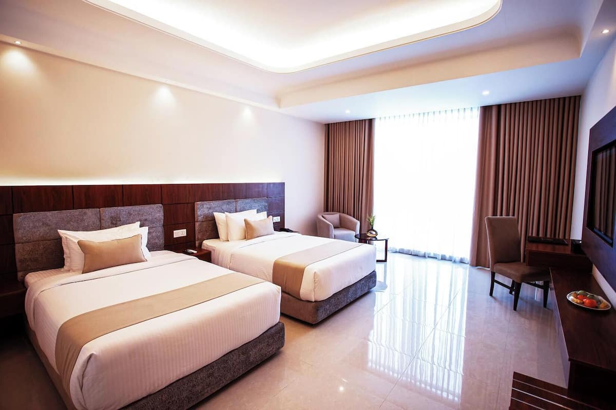 A hotel room with two beds, a desk, a chair, a TV, and a large window with curtains.