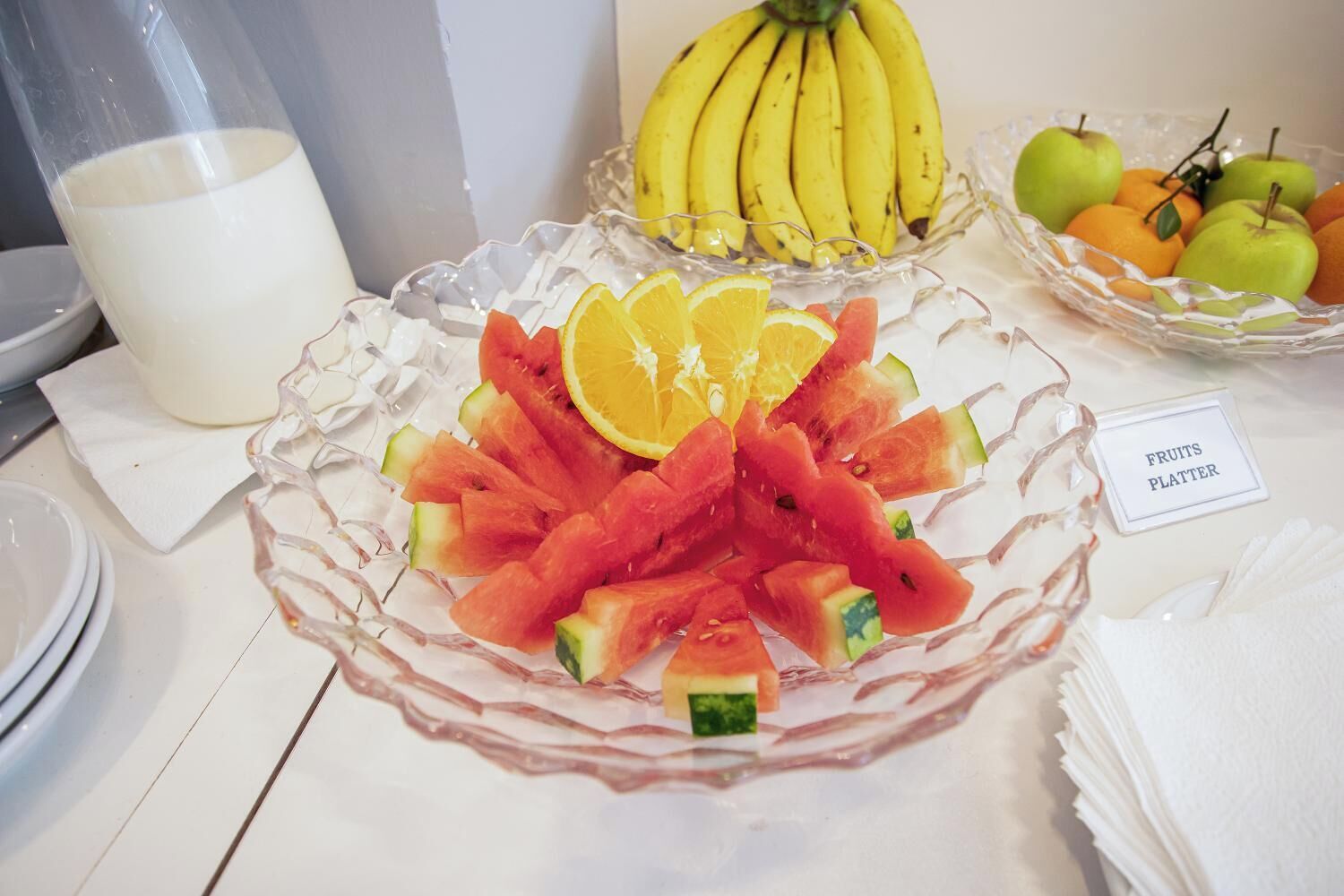Una mesa con una bandeja de frutas, un vaso de leche y un tazón de plátanos.