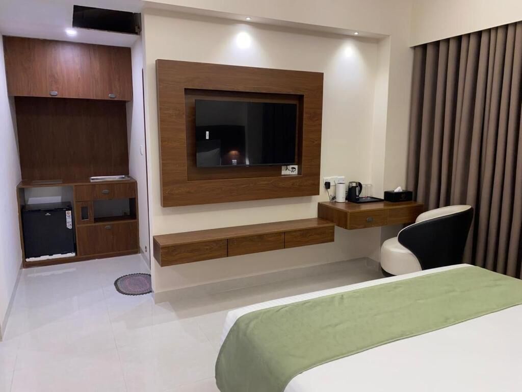 Quarto de hotel com cama, televisão na parede, pequena escrivaninha com cadeira e armário embutido.