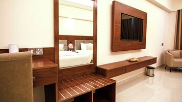 A hotel room with a large mirror, a bed with a headboard, a wooden console table, a small trash bin, and a chair.