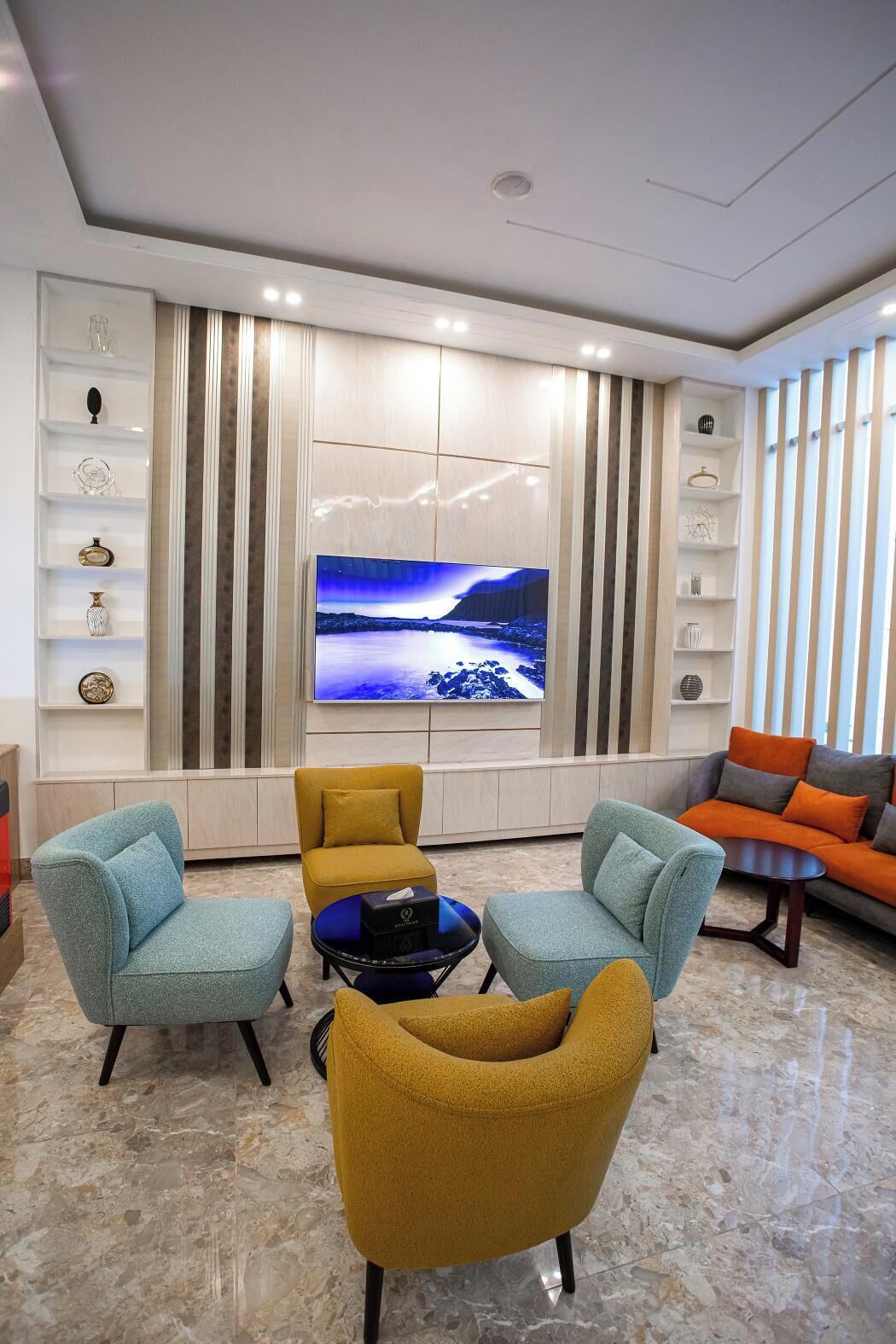 A modern living room with a flat-screen TV, two armchairs, a coffee table, and a sofa.