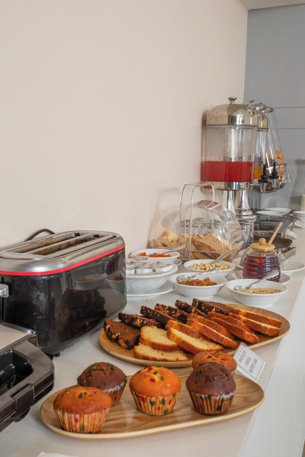 A buffet setup with a toaster, various breads, muffins, and a coffee station.
