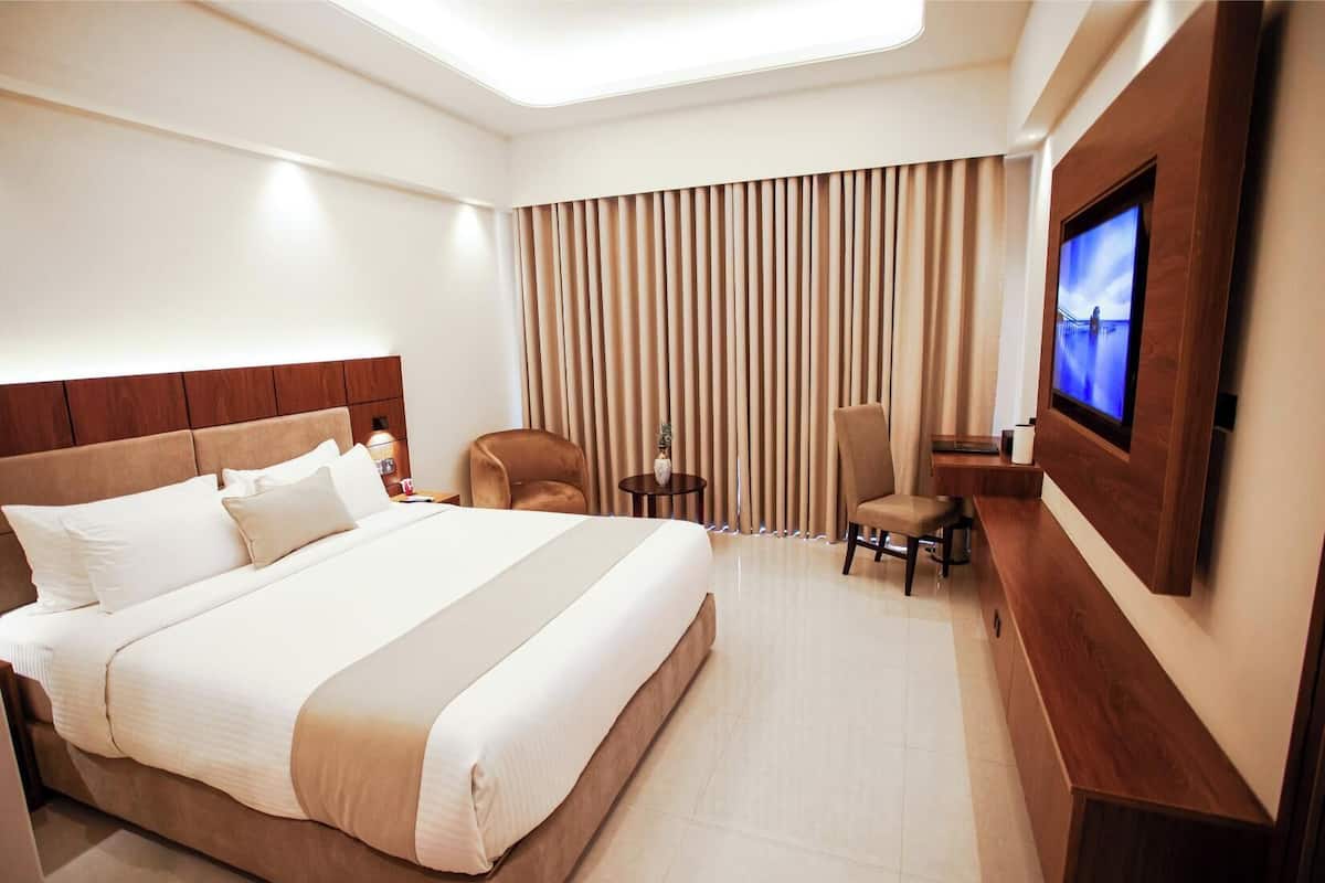 A hotel room with a large bed, a TV mounted on the wall, a desk, and a chair.