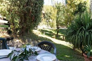 An outdoor dining area with a table set for two, surrounded by lush greenery and trees.