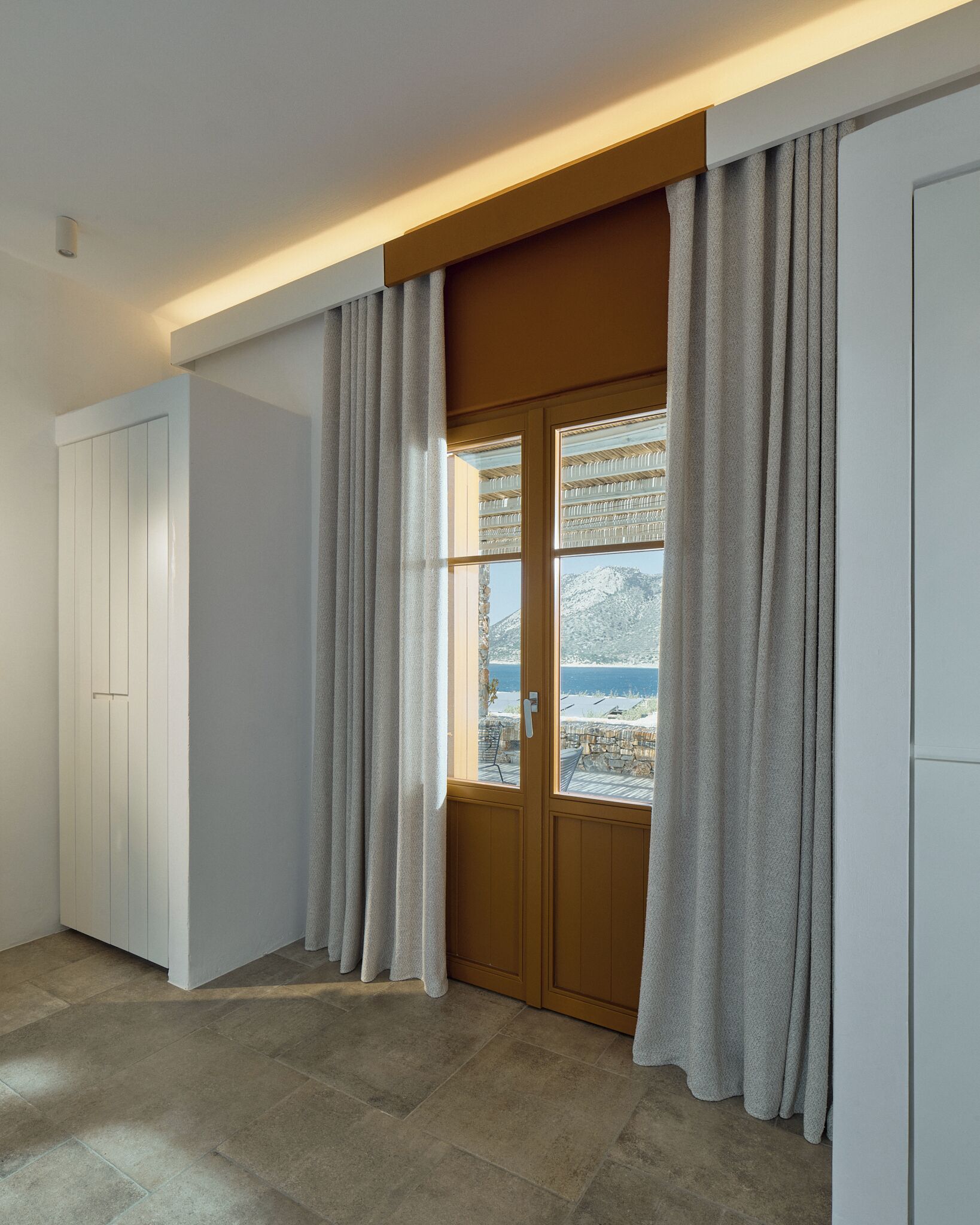 Una habitación con puerta de madera, paredes blancas y vistas a un paisaje montañoso.