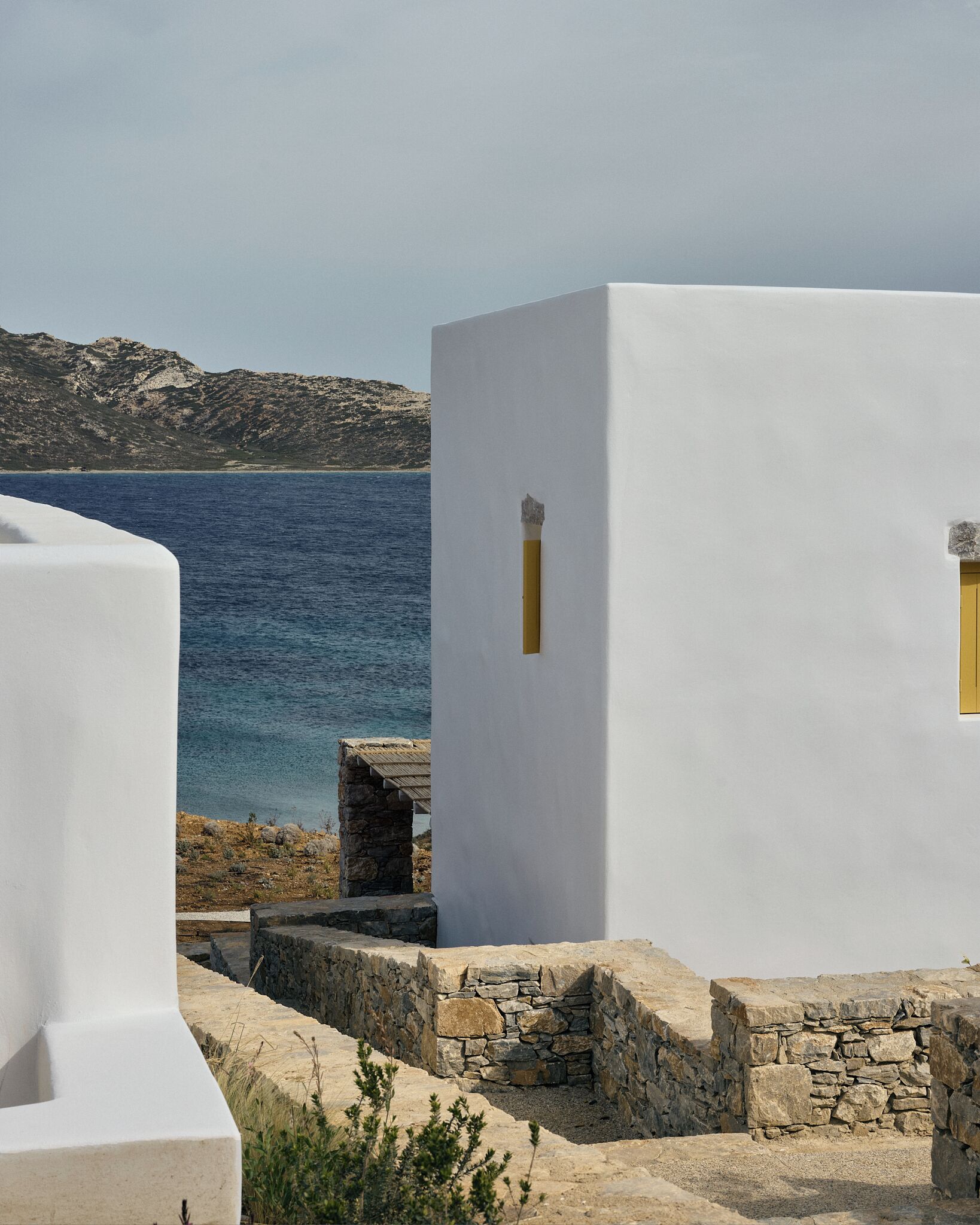 A white building with a stone foundation, a small window, and a view of the sea.