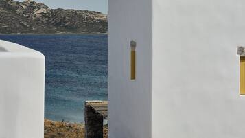A white building with a stone foundation, a small window, and a view of the sea.