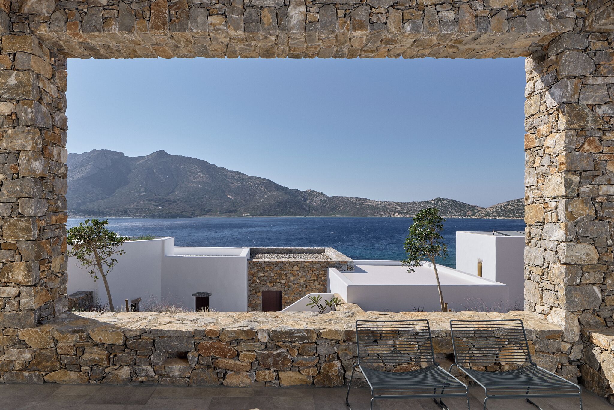 Ventana enmarco de piedra con vistas a un paisaje costero, que incluye una montaña y el mar.