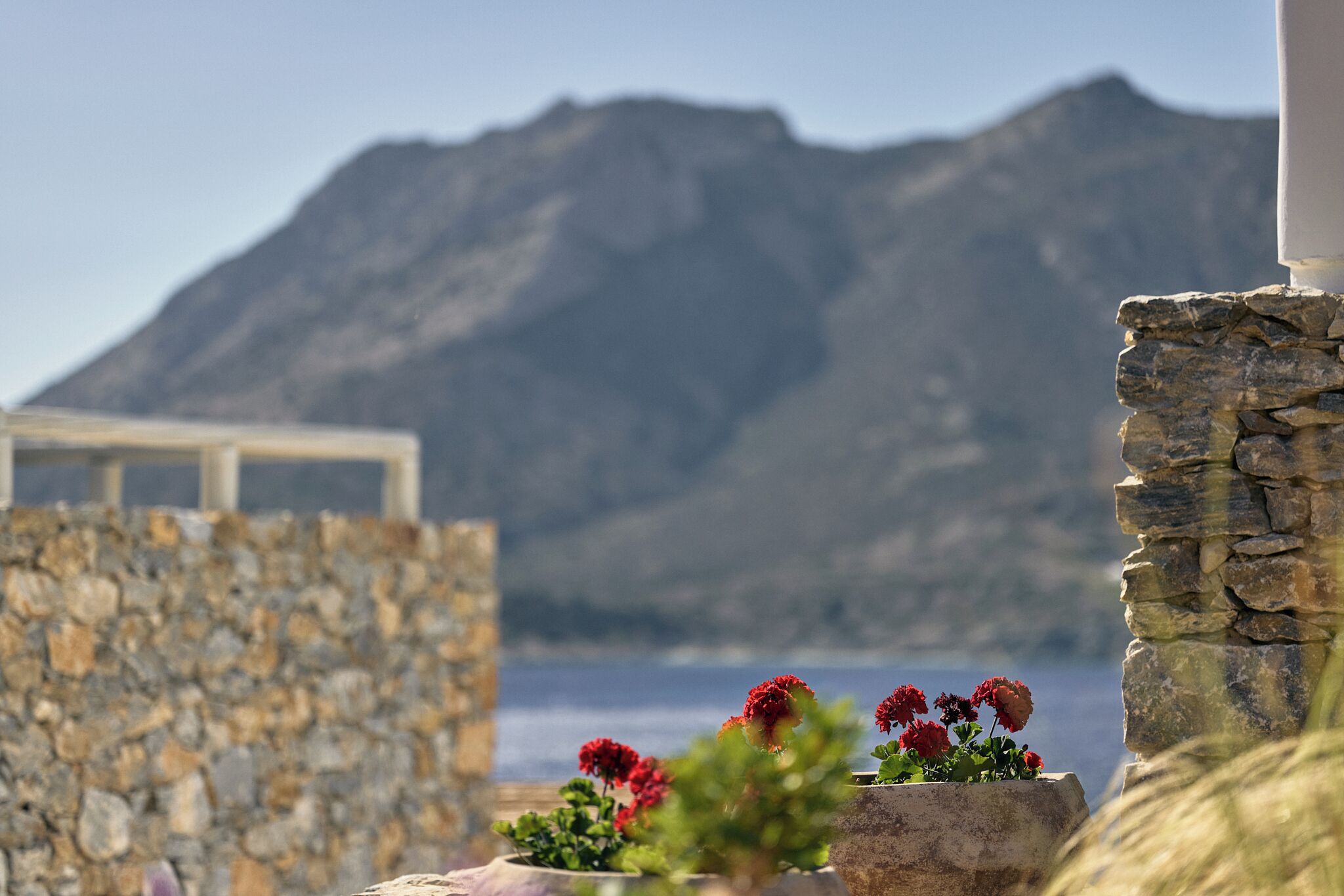 A stone wall with a flower arrangement in the foreground and a mountain in the background.