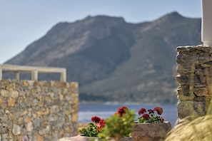 A stone wall with a flower arrangement in the foreground and a mountain in the background. - Amorgina (Amorgos)